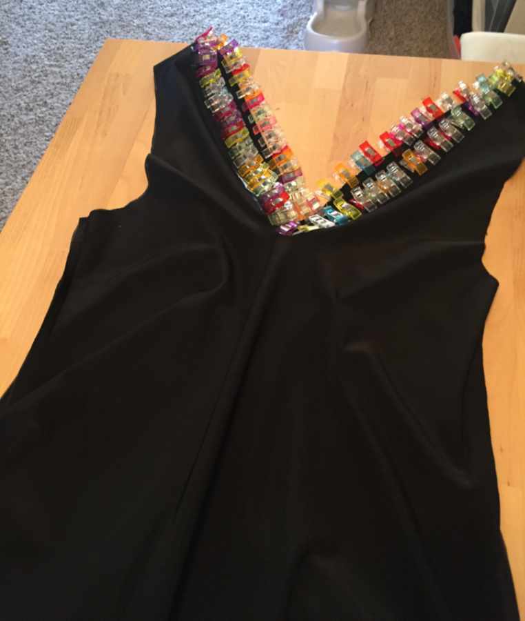 unfinished black dress on a table, the hem of the collar is held down by numerous colorful small clips